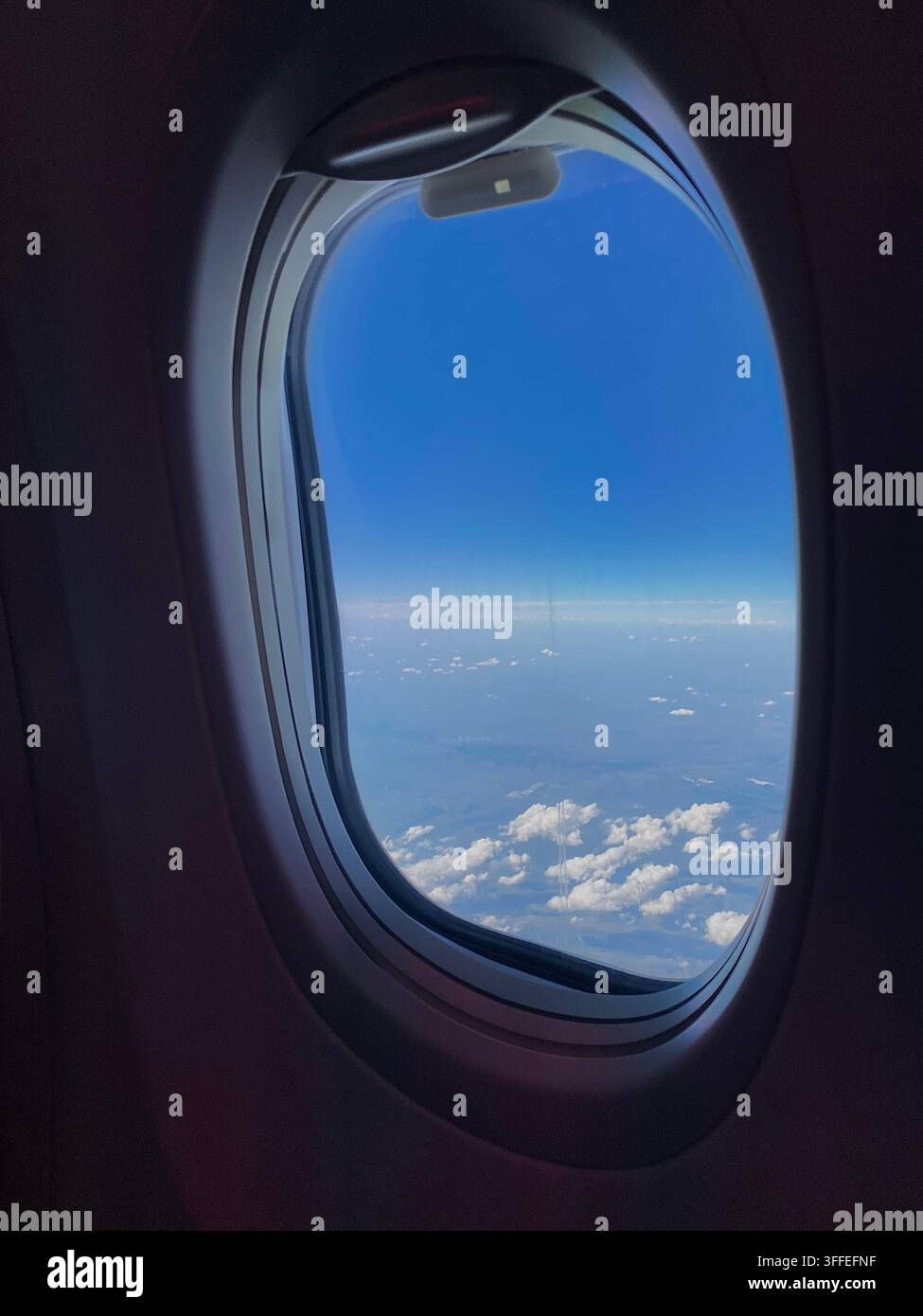 Flugzeugfenster rahmen blauen Himmel und vereinzelte Wolken bei hellem Tageslicht ein. - Smartphone-aufgenommenes Stockfoto