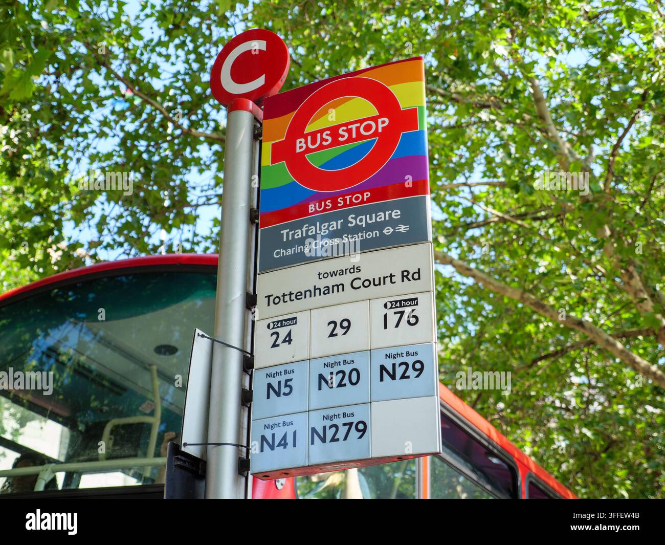 Bushaltestelle, die mit der Regenbogenfahne der Homosexuellenbewegung um das TFL-Rundschild am Traflagar Square, London, UK, geschmückt ist Stockfoto