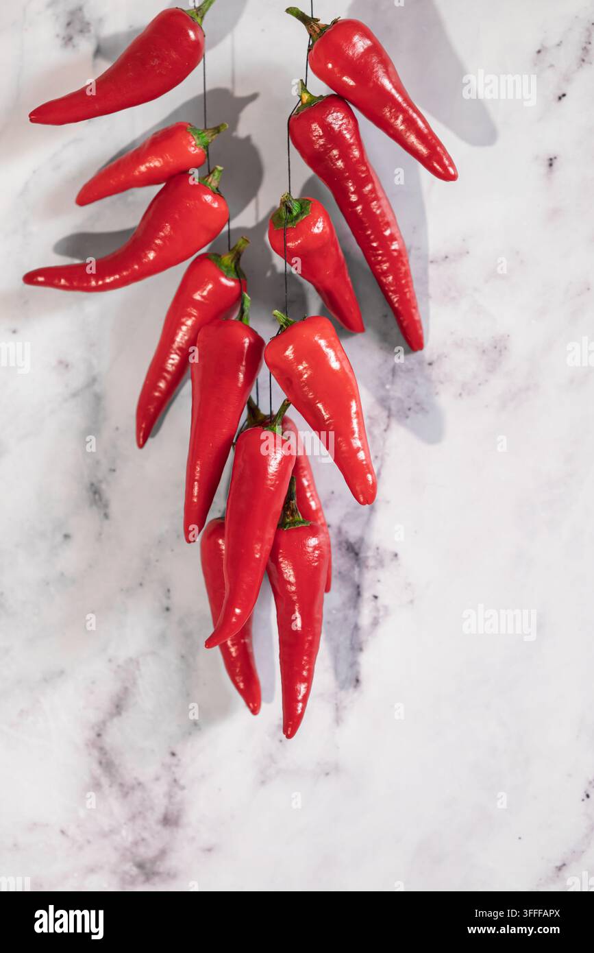 Rote Chilischoten hängen auf hellem Marmor mit harten Schatten Stockfoto