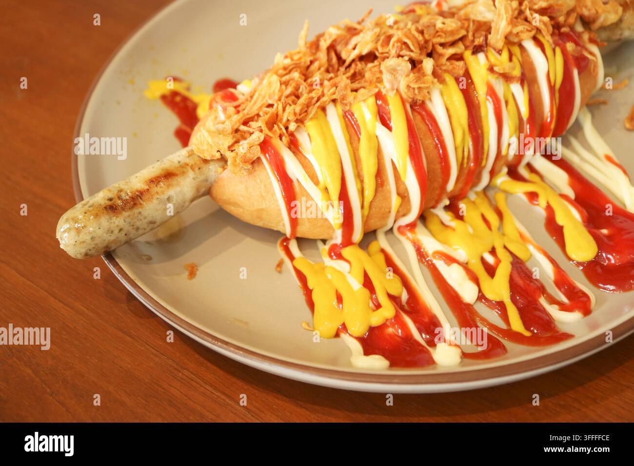 Gourmet-Deutsche Wurst-Hotdog mit knusprigen Zwiebeln und beträufelten Saucen auf einem Teller Stockfoto