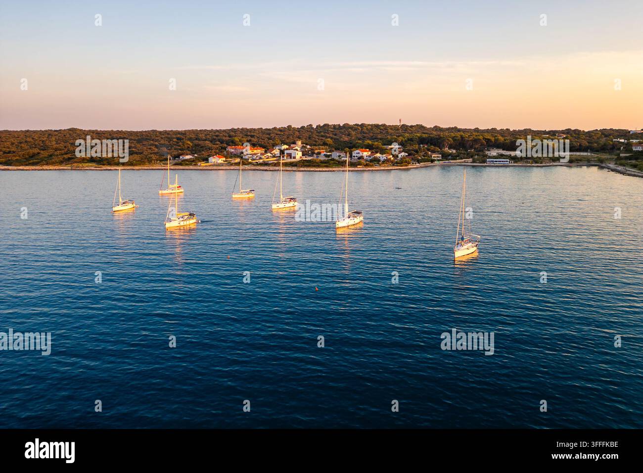Luftaufnahme von Yachten, die bei Sonnenuntergang vor der ruhigen Küste der Insel Silba, Kroatien, vor Anker liegen. Goldenes Sonnenlicht wärmt das ruhige, tiefblaue Adriatische Meer Stockfoto