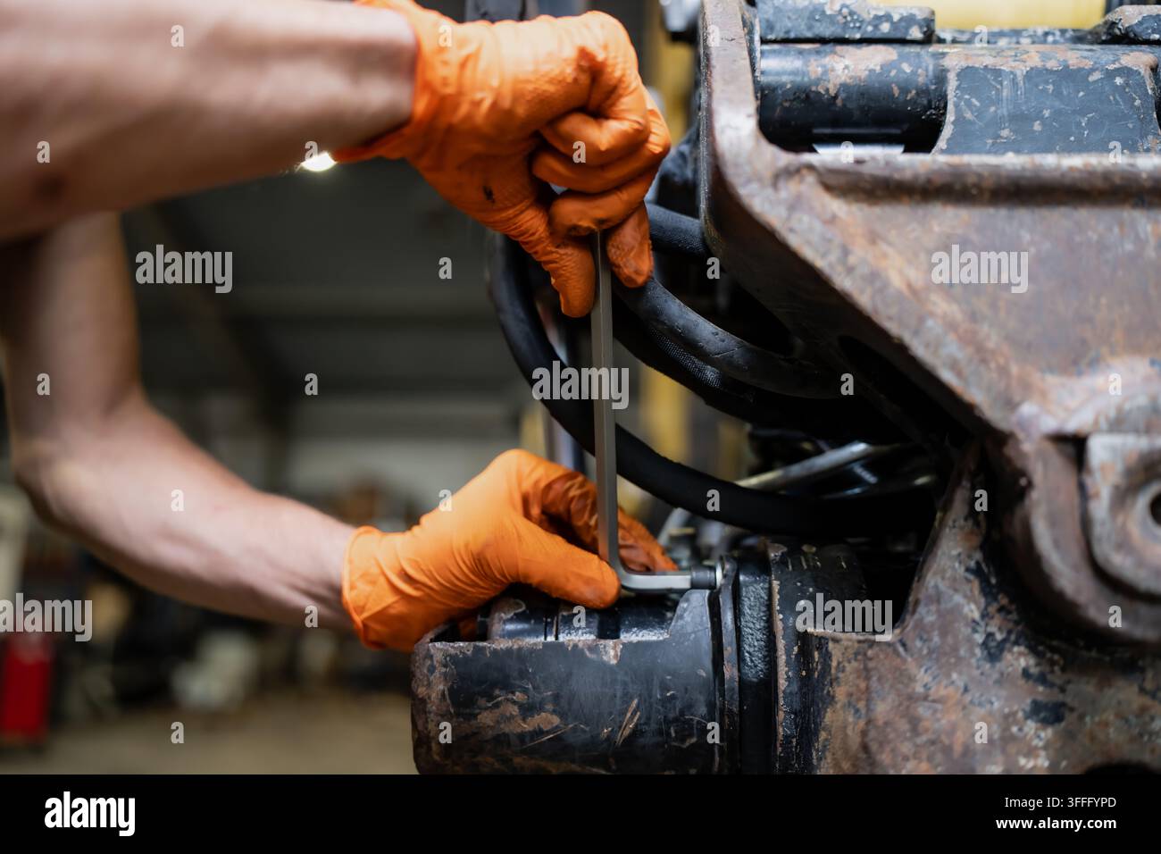 Schützende Handschuhe arbeiten an einem Steckverschluss neben Hydraulikschläuchen und einem Metallmaschinengelenk, was Ausrüstungswartung und Handwerkzeuge darstellt Stockfoto