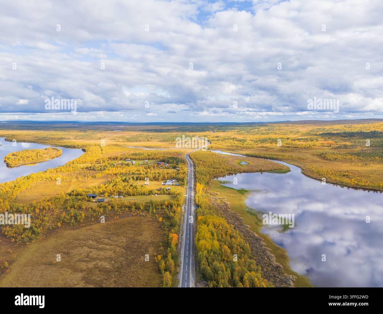 Luftaufnahme einer arktischen Straße, die durch goldene Herbsttundra nahe traditioneller Hütten und einem spiegelnden Fluss im Norden Schwedens führt Stockfoto