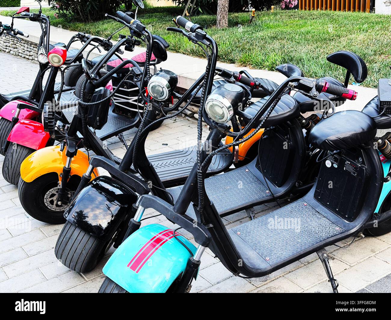 Eine Reihe moderner Elektroscooter mit breiten Reifen, die auf einer Stadtstraße geparkt sind. Helle Farben und stilvolles Design machen dieses umweltfreundliche Fahrzeug attraktiv Stockfoto