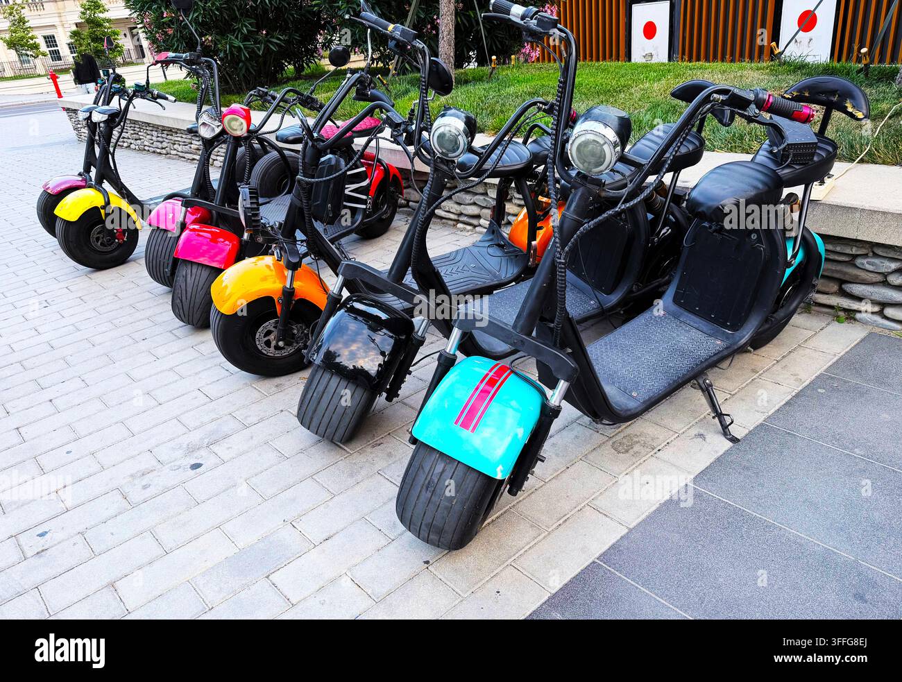 Eine Reihe moderner Elektroscooter mit breiten Reifen, die auf einer Stadtstraße geparkt sind. Helle Farben und stilvolles Design machen dieses umweltfreundliche Fahrzeug attraktiv Stockfoto
