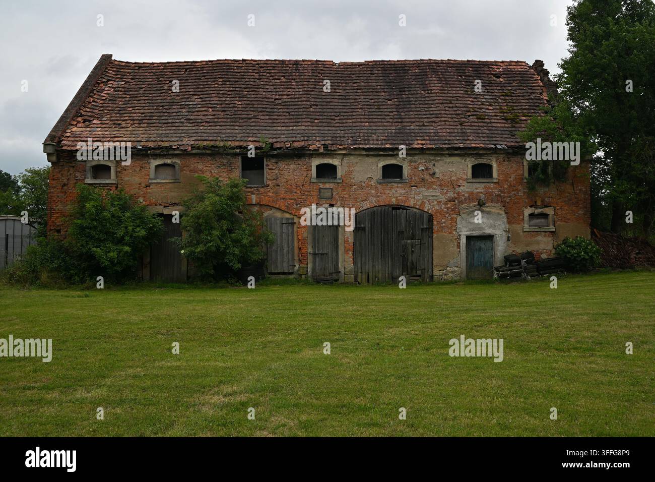 Verlassene rote Backstein-Scheune und historische Bauernhofgebäude unter einem stürmischen Himmel – ländliche Landschaft der Kaczawskie-Füßchen Stockfoto