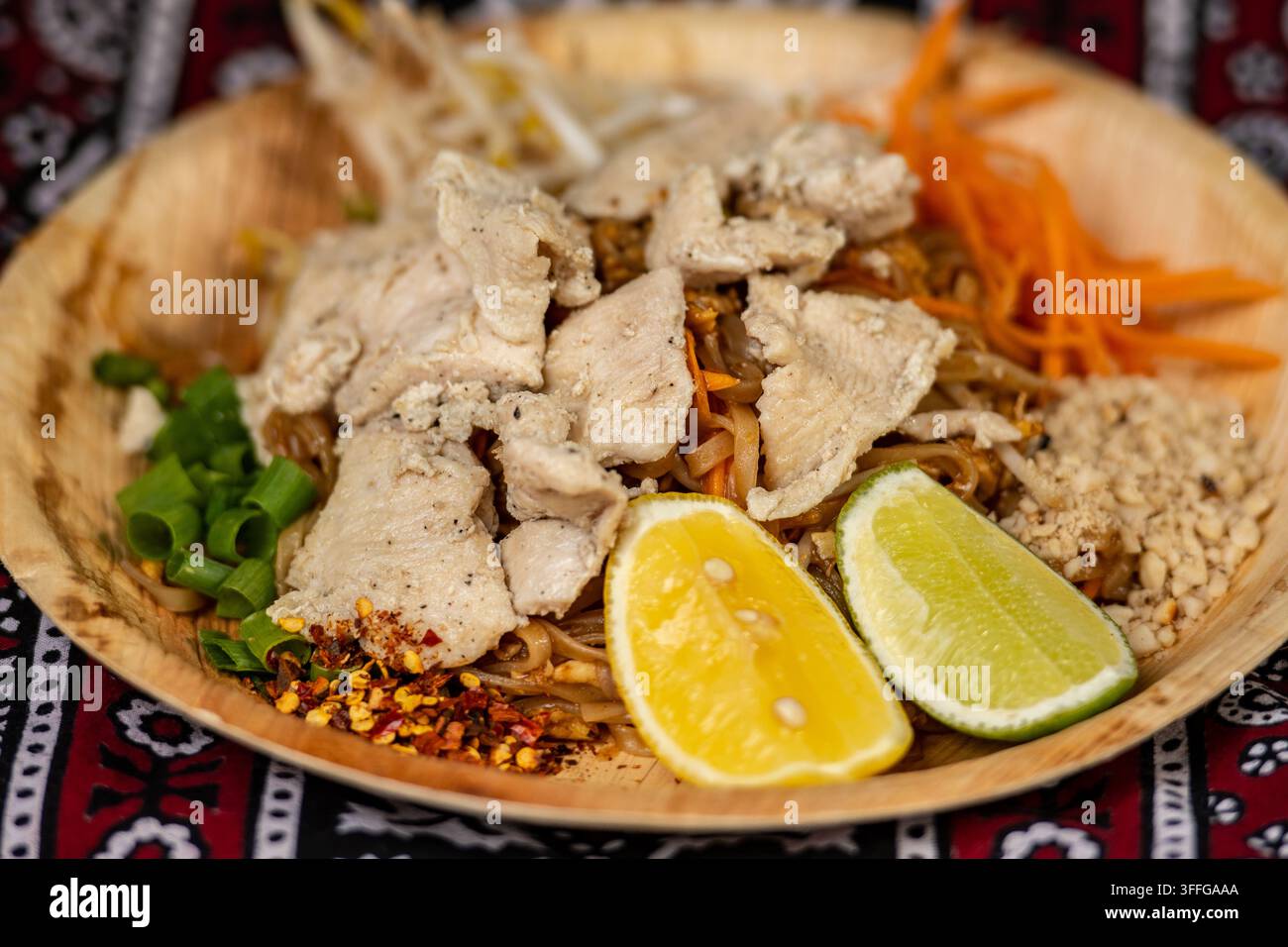 Chicken Pad Thai, ein beliebtes thailändisches Reisnudeln-Gericht, garniert mit geschnittenem Hühnchen, Limette, zerkleinerten Erdnüssen und Frühlingszwiebeln Stockfoto