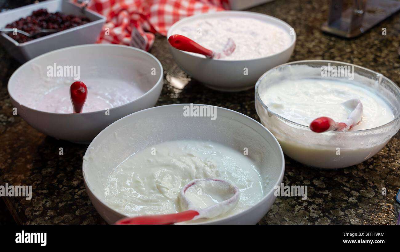 Schüsseln mit Joghurt an einem Hotel-Frühstücksbuffet mit Servierlöffeln Stockfoto