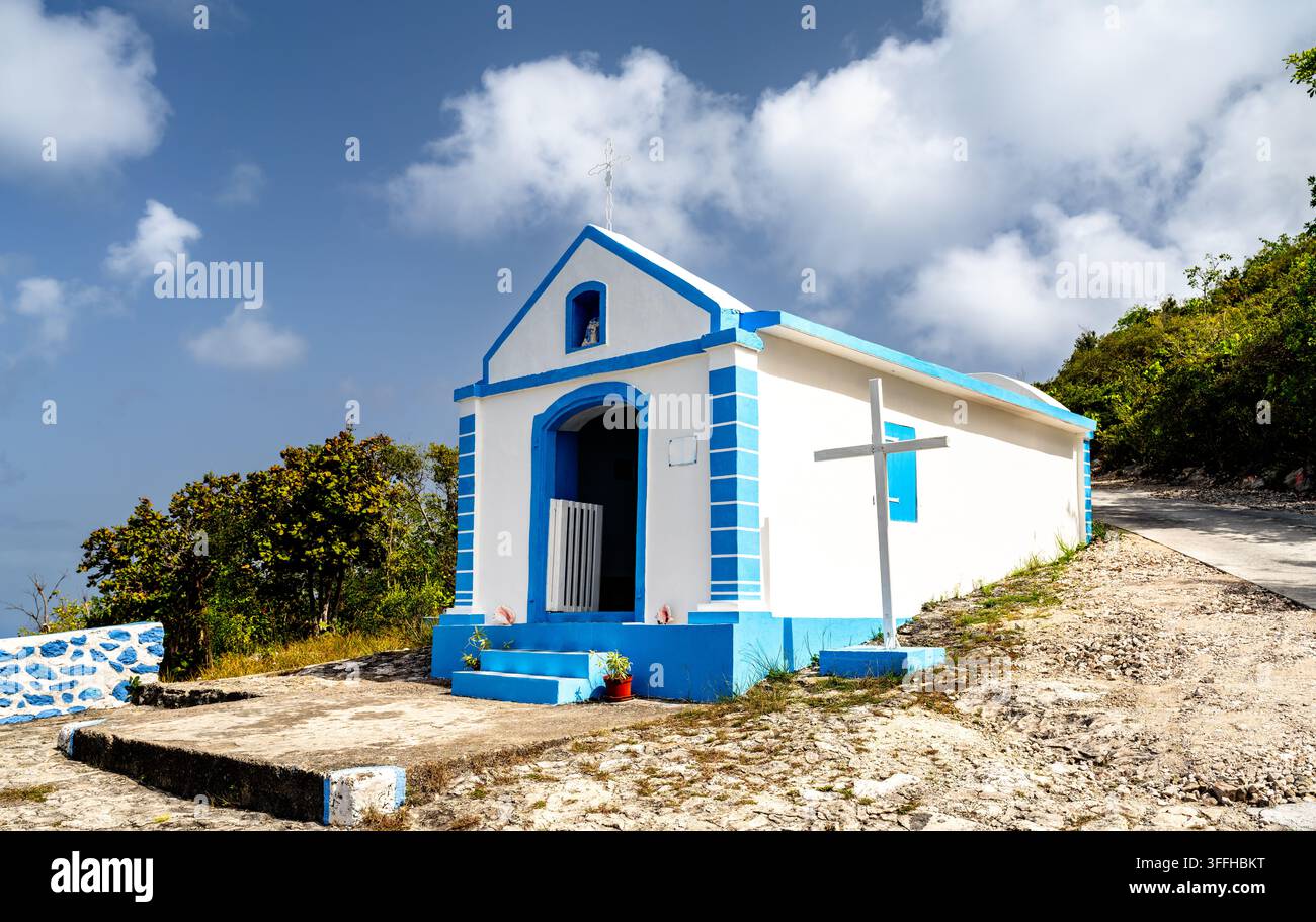 Kleine weiß-blaue Kapelle Notre Dame du Calvaire auf einem Hügel in La Desirade, Guadeloupe, vor einem bewölkten Himmel. Stockfoto