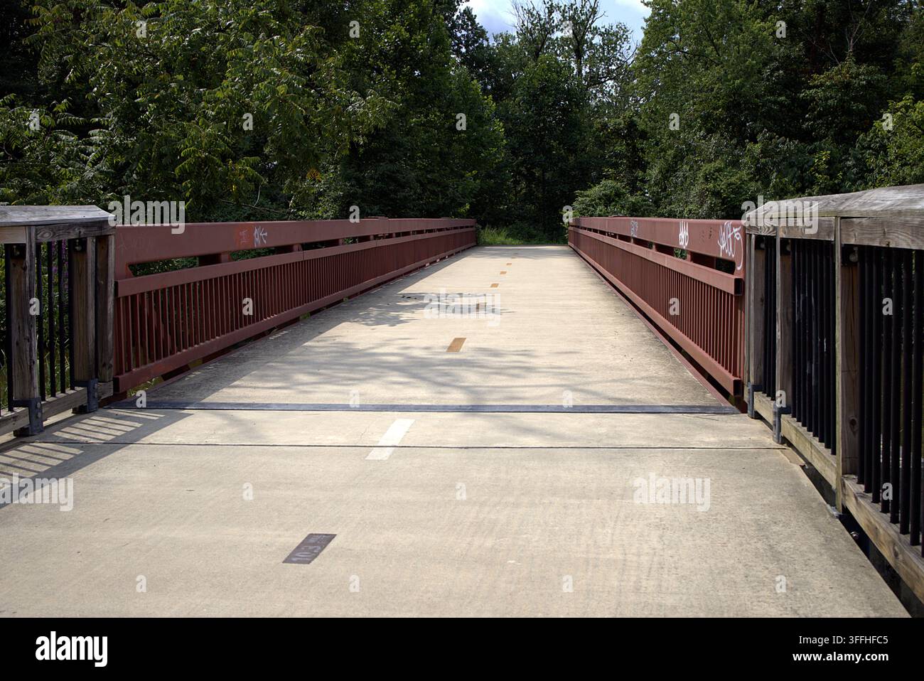Ein Weitwinkel-, symmetrisches Landschaftsfoto, das auf eine leere gepflasterte Fußgänger- und Fahrrad-Multifunktionswegbrücke hinunterblickt. Stockfoto