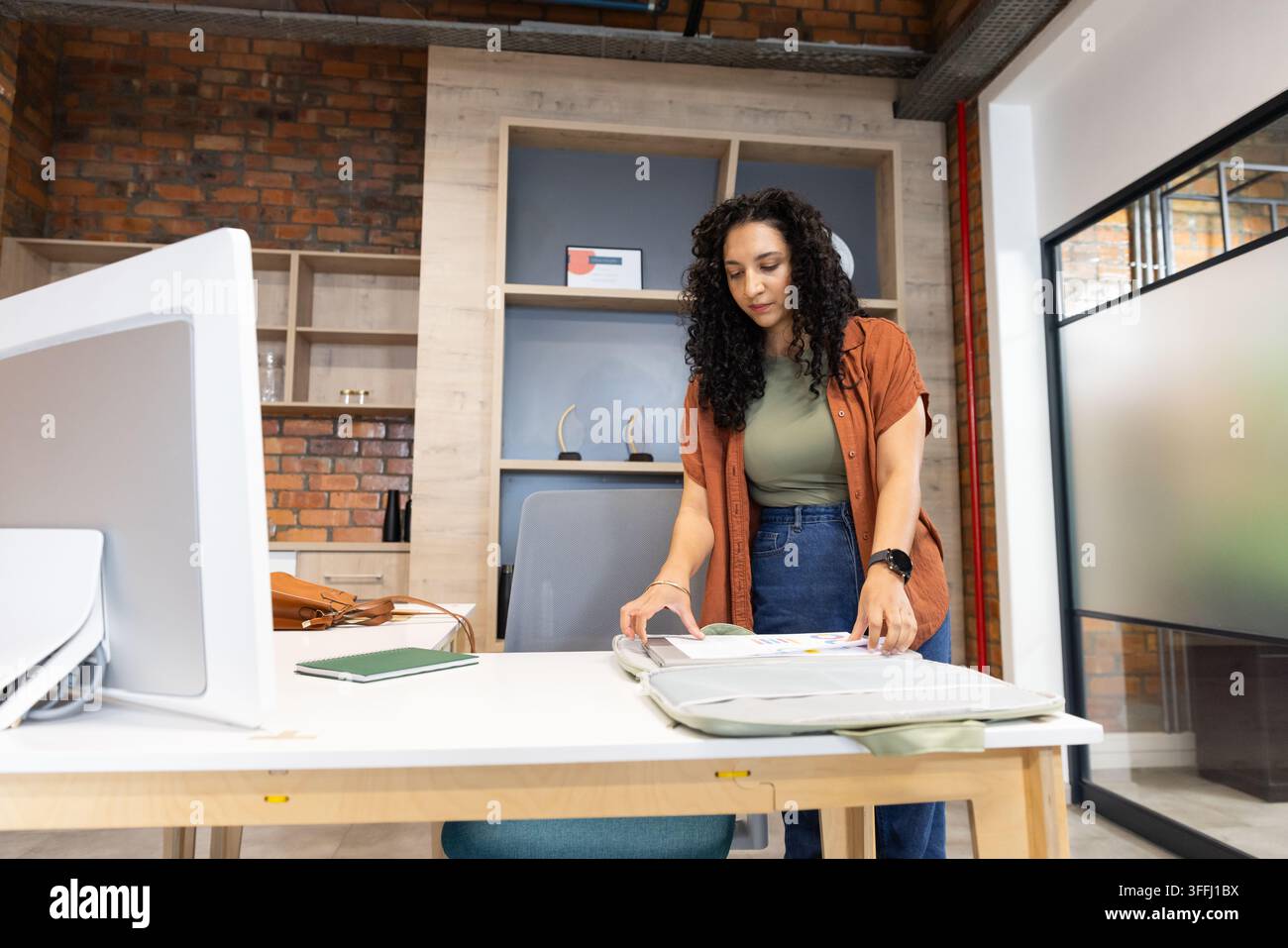 Afrikanische Frau, die rechts an einem hellen Holzschreibtisch steht und ein offenes Portfolio mit Monitor durchsieht Stockfoto