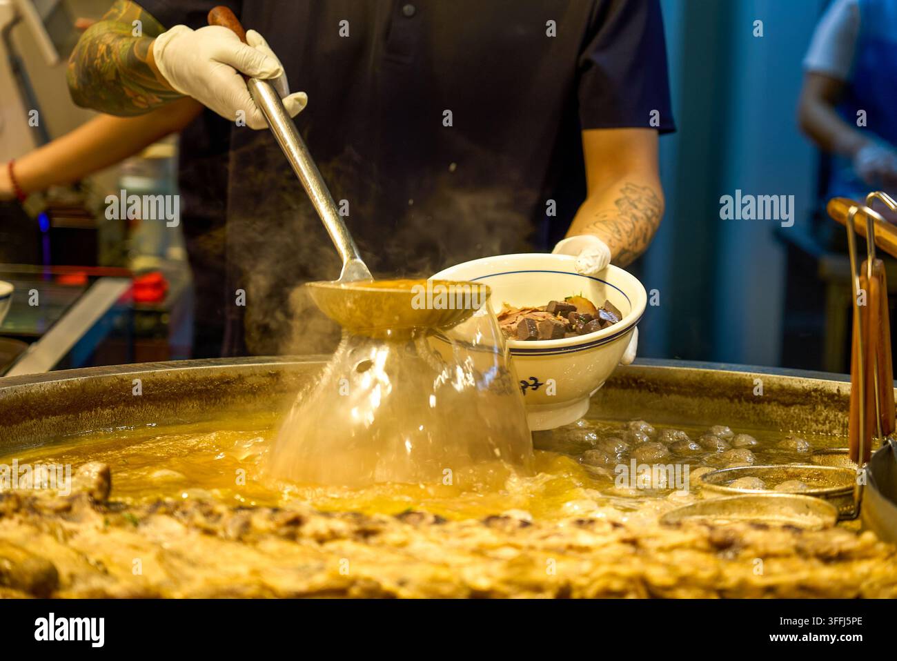 Rindfleischsuppe fließt wie ein Wasserfall aus einem großen Löffel, und Dampf erfüllt den Guizhou-Rindfleisch-Nudelnstand. Stockfoto