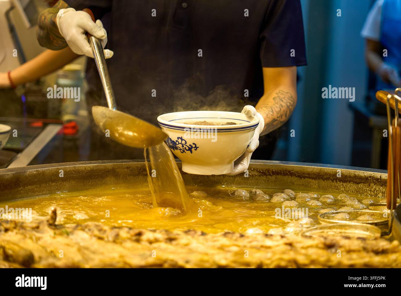Der Besitzer des Guizhou-Rindernudeln-Stands schöpft die Suppe aus, während er eine Schüssel hält, und gießt die heiße Brühe in die Schüssel. Stockfoto