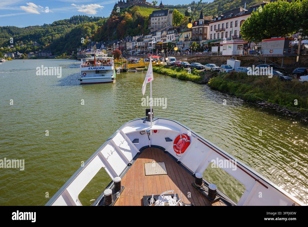 Blick vom Bug eines Passagierkreuzfahrtschiffs auf einen malerischen europäischen Fluss mit einem weiteren Boot voraus und einer historischen Stadt entlang des Ufers an einem sonnigen Tag Stockfoto