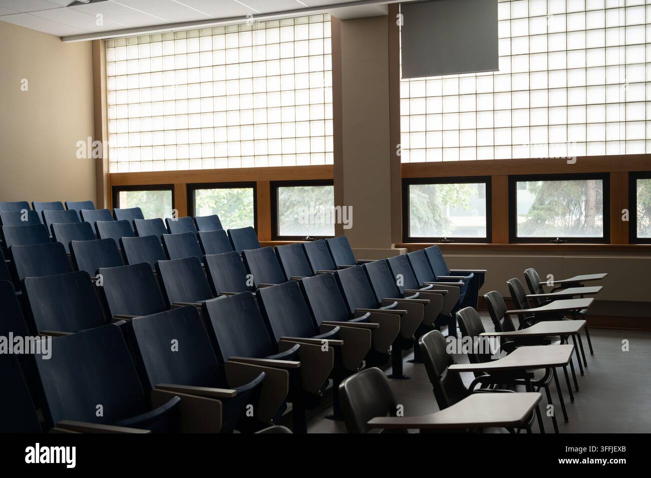 Reihen fester blauer, gestufter Theatermöbel treffen auf bewegliche Tischarm-Stühle im hinteren Teil eines leeren Hörsaals im Isbister-Gebäude der U Stockfoto