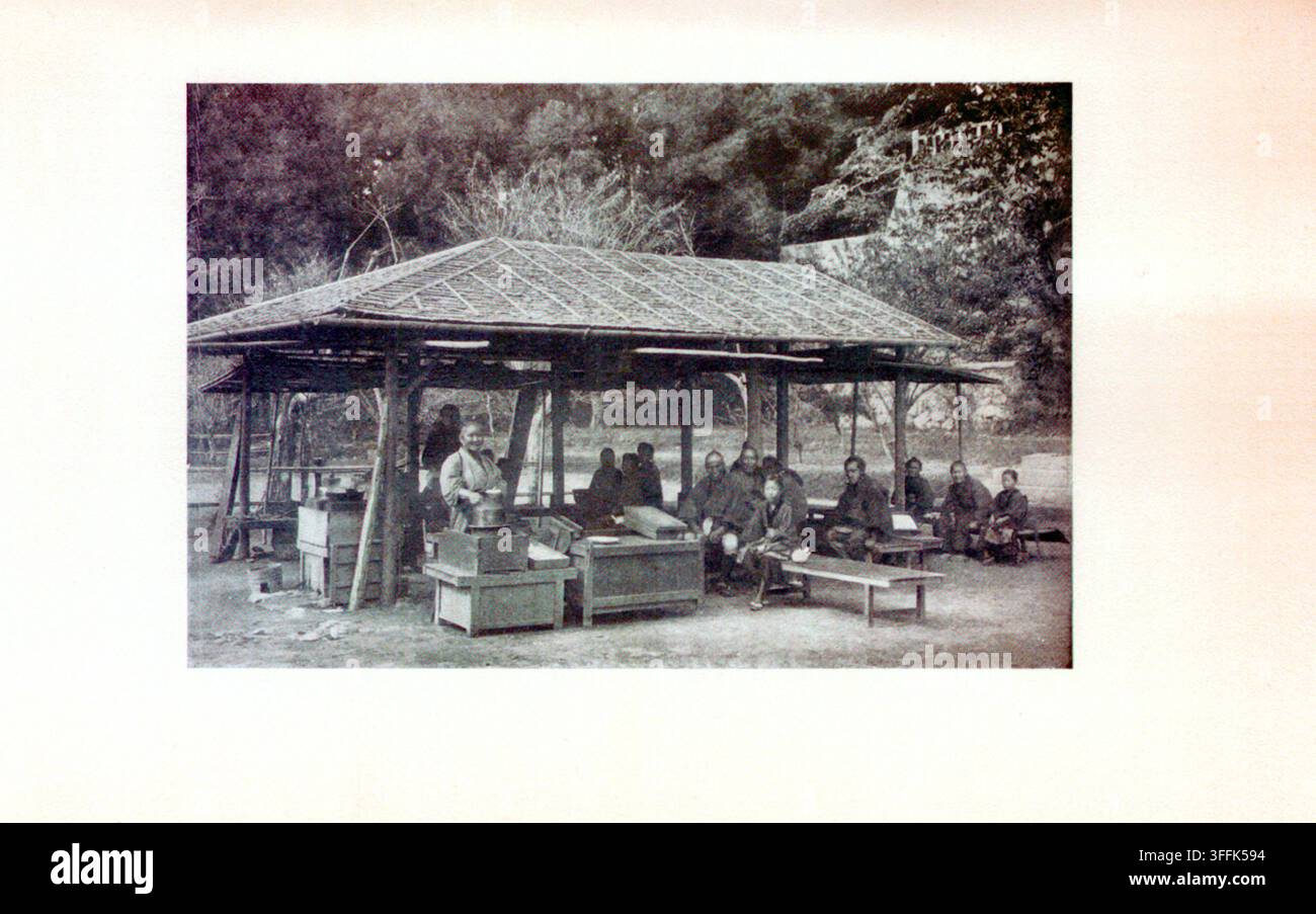 Kunst und Kultur Japans. Rastplatz am Wegesrand. 1904 Diese sepiafarbene Fotografie fängt einen ruhigen Moment an einem traditionellen japanischen Rastplatz (hatago chaya) ein – einem bescheidenen Straßenschild, an dem müde Reisende eine Pause für Erholung, Erfrischung und eine warme Mahlzeit einlegen konnten. Solche Schutzhütten waren während der Edo- und frühen Meiji-Zeit weit verbreitet, insbesondere entlang wichtiger Reisewege wie dem Tōkaidō, und boten Samurai, Händlern, Pilgern und Bauern, die zu Fuß unterwegs waren, eine vorübergehende Erholung. Die Struktur ist einfach, aber funktional – aus natürlichem Holz und Stroh gebaut, mit einem offenen Grundriss, der prom Stockfoto
