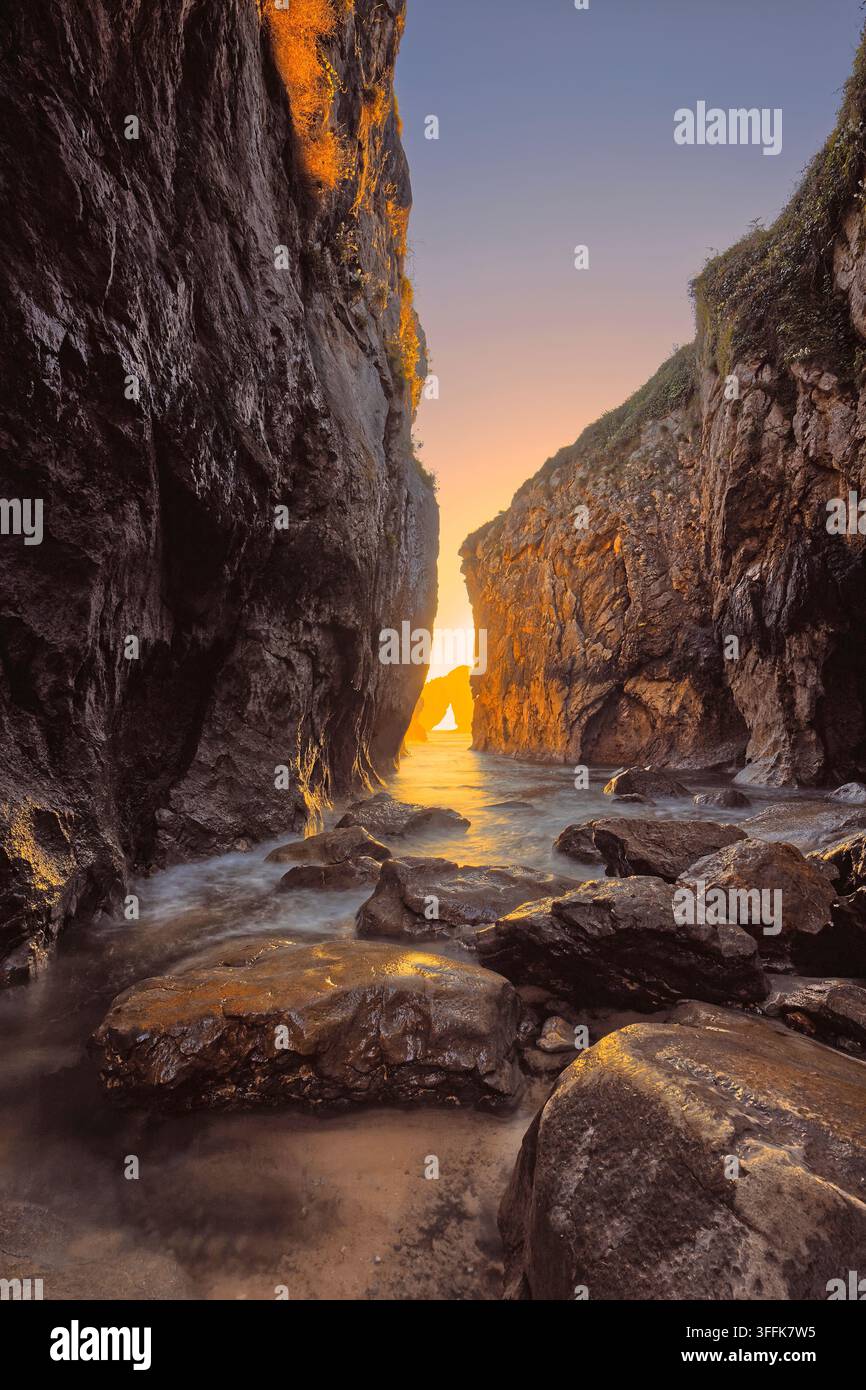 088 Gezeitenanstieg in der engen, mit Felsen übersäten Playa la Canalina Beach, die von einem feurigen Morgengrauen über der Insel Castro de las Gaviotas begleitet wird. Llanes-Asturien-Spanien Stockfoto