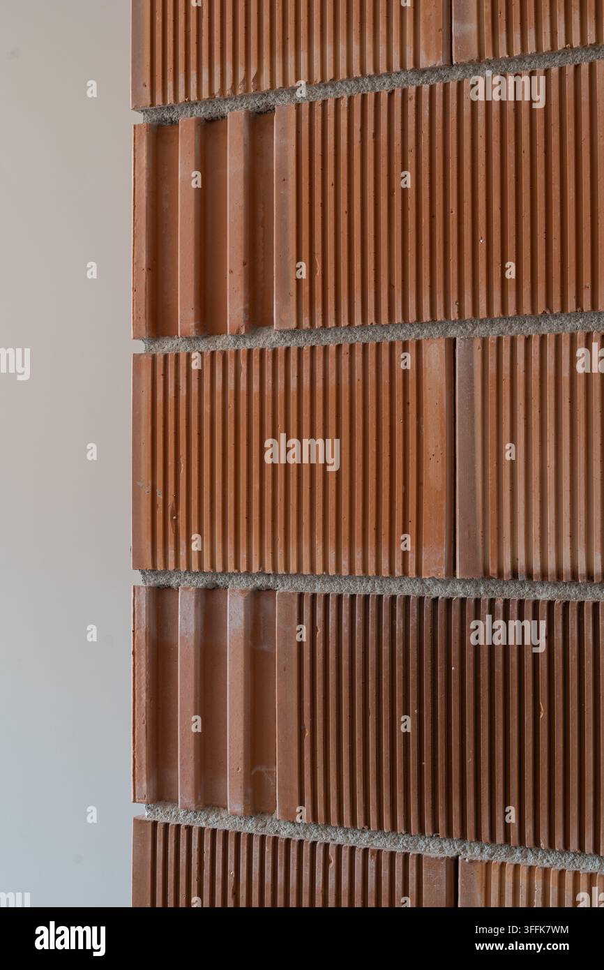 Strukturierte Terracotta-Ziegelwand mit abwechselnden glatten und gerippten Schichten, vertikalen Rillen, Mörtelfugen, warmen Erdtönen und sich wiederholendem Muster Stockfoto