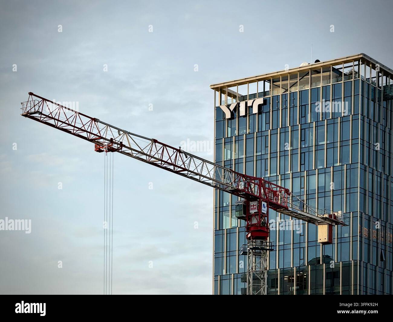 Niedrigwinkelfoto eines roten Baukranauslegers, der an einem modernen Hochhaus aus Glas in Vilnius, Litauen, vorbeiläuft und das YIT-Unternehmenslogo zeigt. Stockfoto