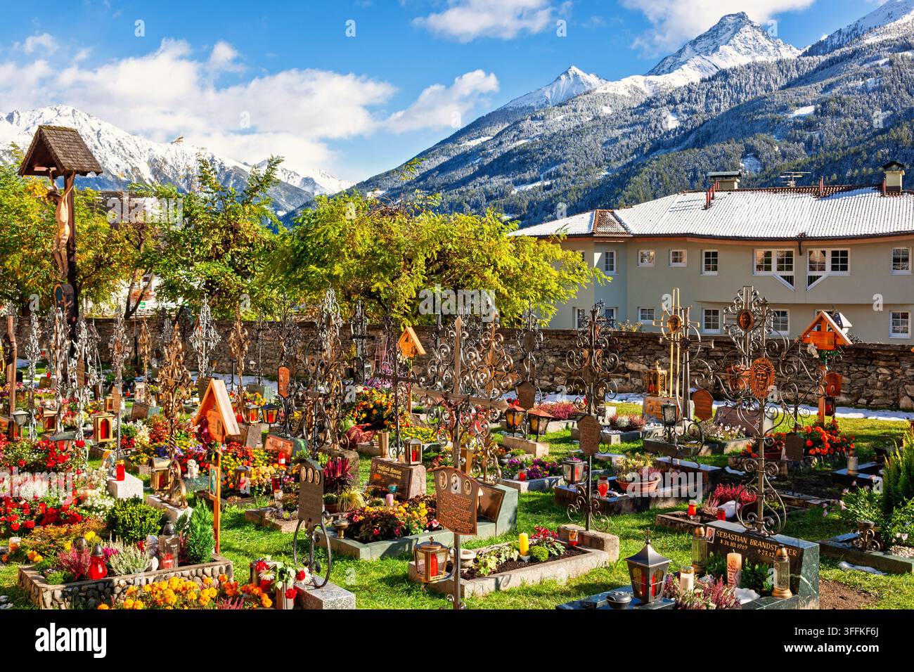 Kirchhof in Österreich mit kunstvollen schmiedeeisernen Grabkreuzen, bunten Blumen in einer Alpenlandschaft Stockfoto