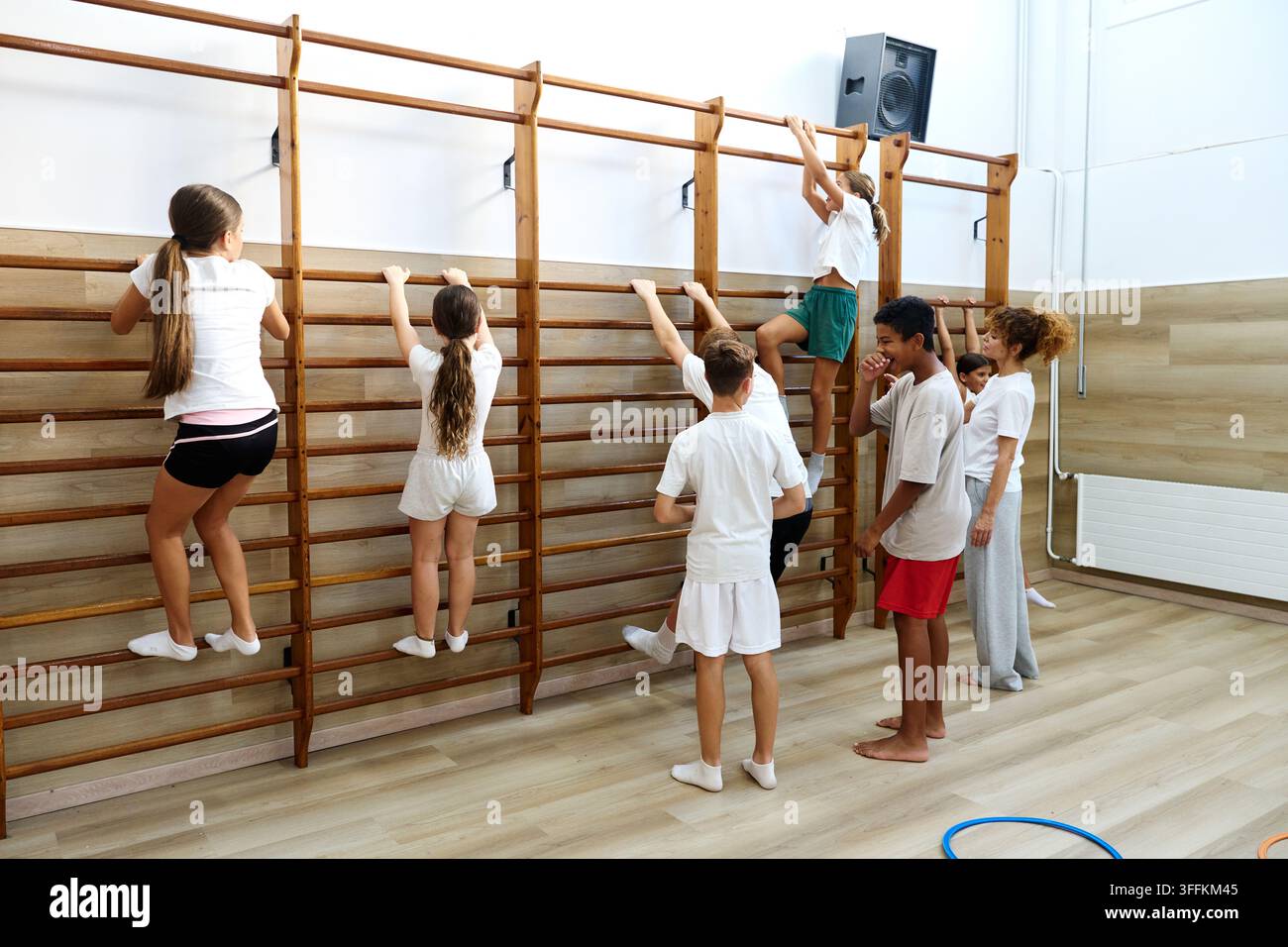 Verschiedene Schüler beschäftigen sich mit Sport, klettern und hängen an Wandstangen in einer Schulturnhalle. Sport und Fitness üben Stockfoto