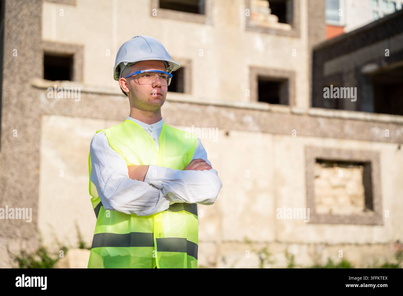 Selbstbewusster Bauprofi trägt Sicherheitshelm und Warnweste auf einer unfertigen Baustelle. Ingenieurüberwachung, Baustellenmanagement und Stockfoto