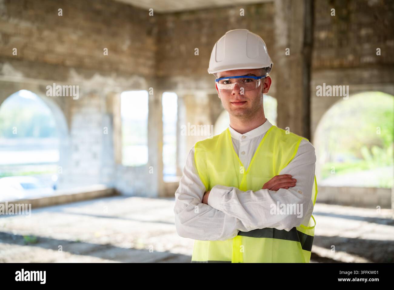Bauleiter steht mit verschränkten Armen in einem unfertigen Betongebäude während der Renovierung. Projektmanagement Ingenieurüberwachung a Stockfoto