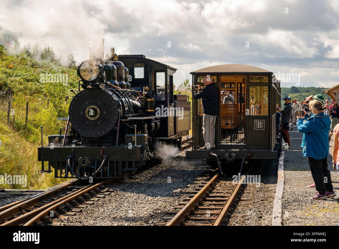 Eine historische Dampflokomotive lässt Dampf ab, während sich Passagiere und Enthusiasten auf dem Bahnsteig versammeln, um die Szene zu fotografieren Stockfoto