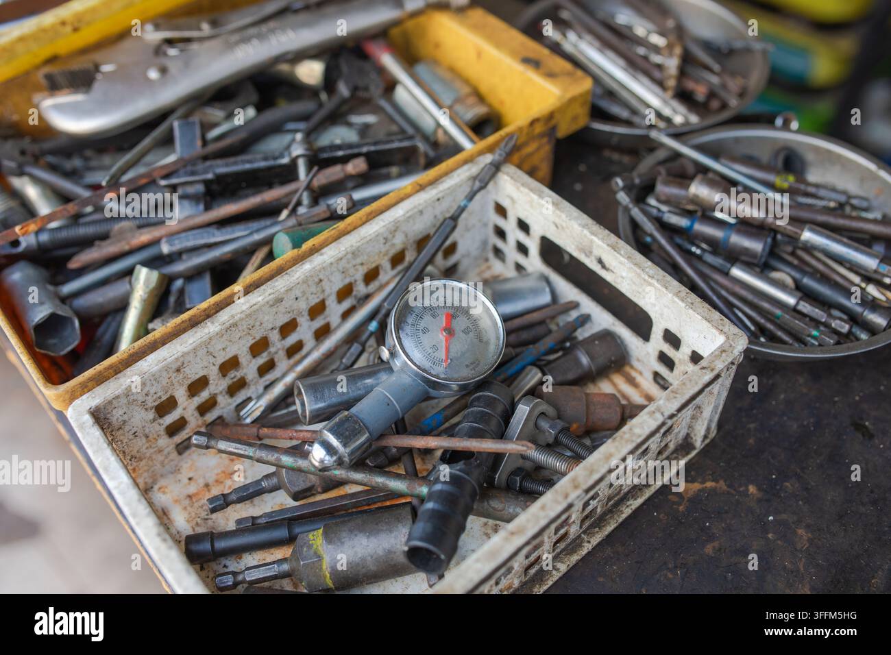 Druckmessgerät liegt zwischen verstreuten Schraubenschlüsseln und Steckdosen in einer Plastikbox, abgenutzte Werkstatts Werkzeuge zeigen Jahre häufiger Nutzung, bereit für Reparaturarbeiten bei Stockfoto