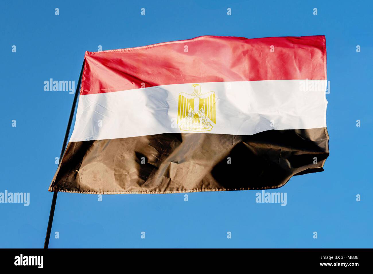 Flagge Ägyptens. Fahne, die im Wind vor einem klaren blauen Himmel weht, flatternd auf einem Flaggenmast im Freien. Heller Sonnentag, Stofftextur, Nahaufnahme im Freien Stockfoto