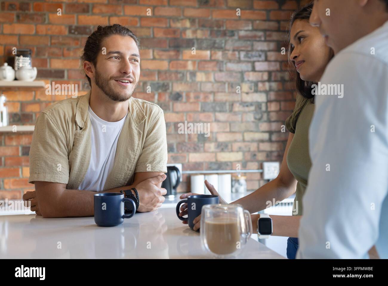 Kollegen lehnen sich an einen weißen Tresen, reden bei Kaffee mit blauen Tassen, Latte, Wasserkocher, Kopierraum Stockfoto