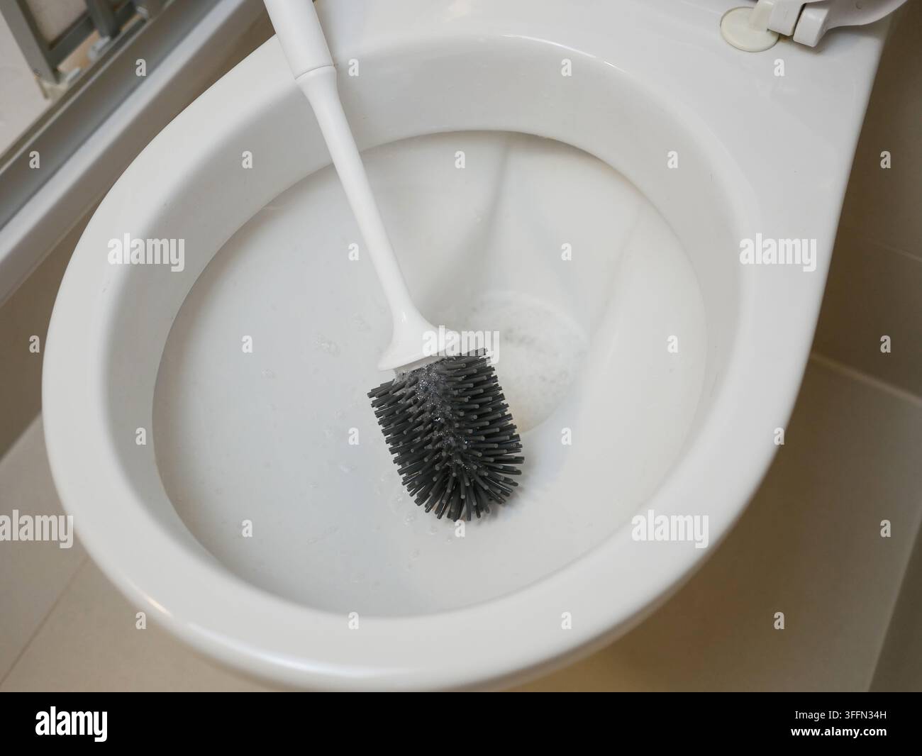 Nahaufnahme einer weißen Toilettenschüssel mit schwarzem Silikon-Bürstenkopf und Schaum - Konzept für Reinigung, Hygiene und Badfrische Stockfoto