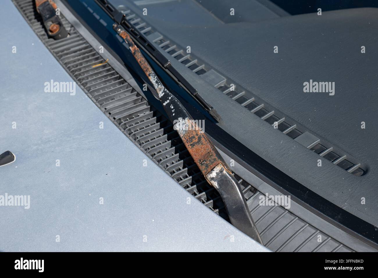 Detaillierte Nahaufnahme von starker Rost- und Lackkorrosion an einem Scheibenwischerarm, der unterhalb der Frontscheibenhaube montiert ist. Stockfoto