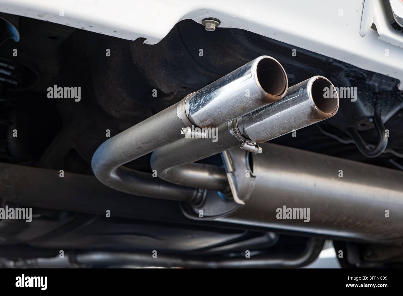 Niedrigwinklige Detailaufnahme von zwei chromfarbenen Auspuffspitzen, die unter der hinteren Stoßstange eines Autos an einen Edelstahl-Schalldämpfer angeschlossen sind. Stockfoto