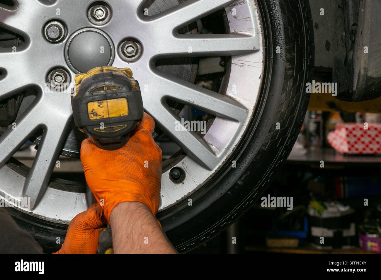 Automechaniker verwendet einen Akkuschlag Schraubenschlüssel, um Radmuttern an einem Autowheel während der Kfz-Reparatur und -Wartung anzuziehen oder zu lösen. Die Nahaufnahme-Werkstatt Stockfoto