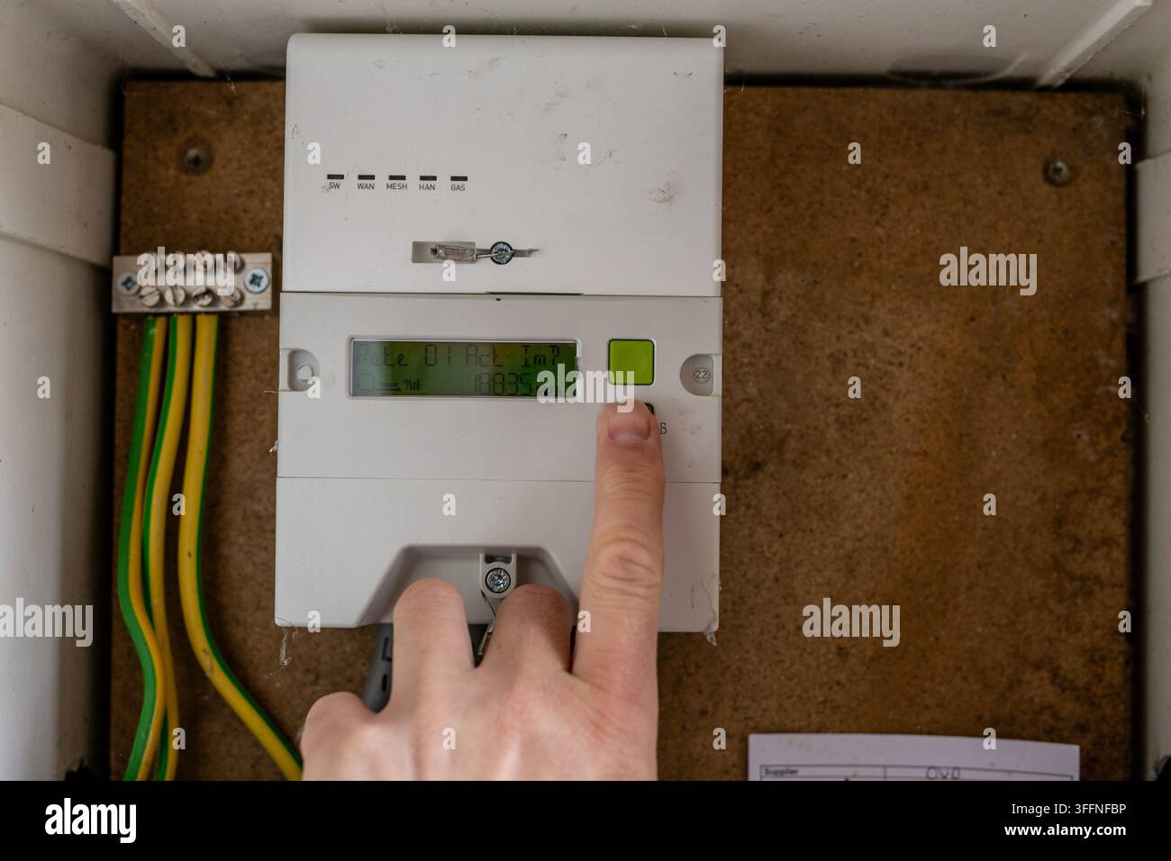 Person drückt eine Taste auf einem Stromzähler für Wohnhäuser, um Informationen zu prüfen oder auf die vom Zähler angezeigten Daten zuzugreifen. Die Nahaufnahme veranschaulicht Haushalts- Stockfoto