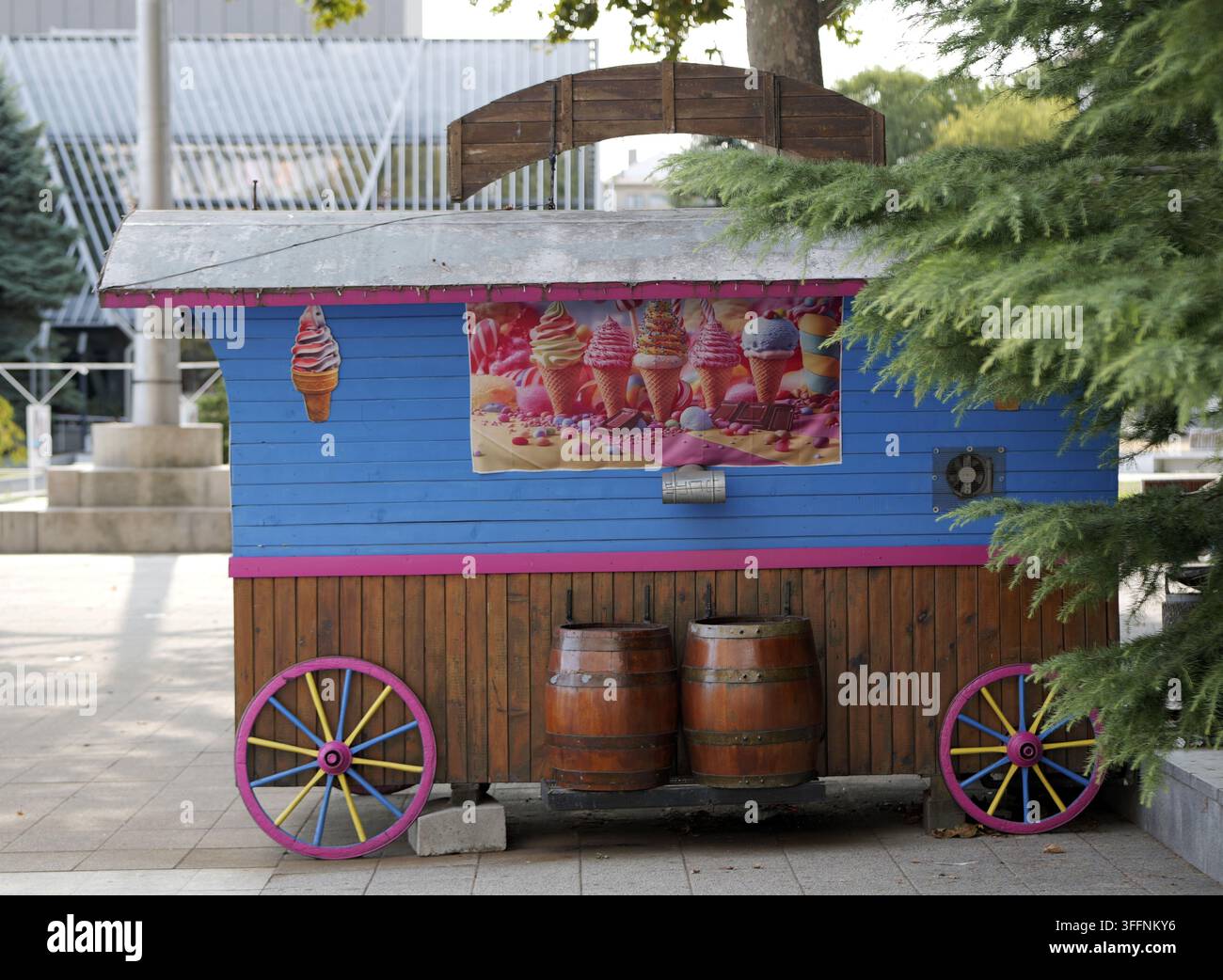 Blauer und rosa Eiswagen mit Holzfässern und farbenfrohen Rädern, der im Freien in einem öffentlichen Park steht und bereit ist, kühle Leckereien während des Krieges zu verkaufen Stockfoto