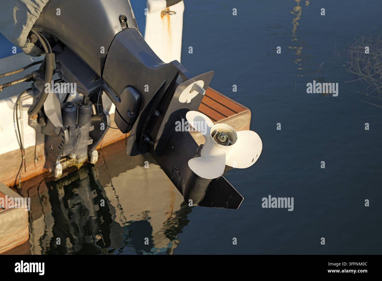 Außenbordmotor mit weißem Propeller, der an einem Bootsrumpf befestigt ist, teilweise in dunklem blauem Wasser eingetaucht, das Licht reflektiert und Wasserfortbewegung ermöglicht Stockfoto