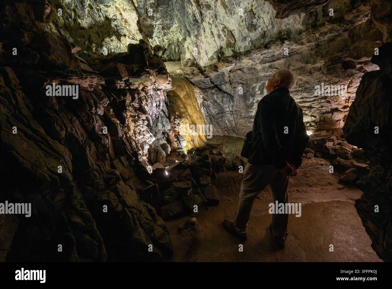 Ein einsamer Entdecker blickt nach oben zu atemberaubenden geologischen Formationen in einer schwach beleuchteten Höhle und betont die natürliche Schönheit der unterirdischen Landschaft Stockfoto