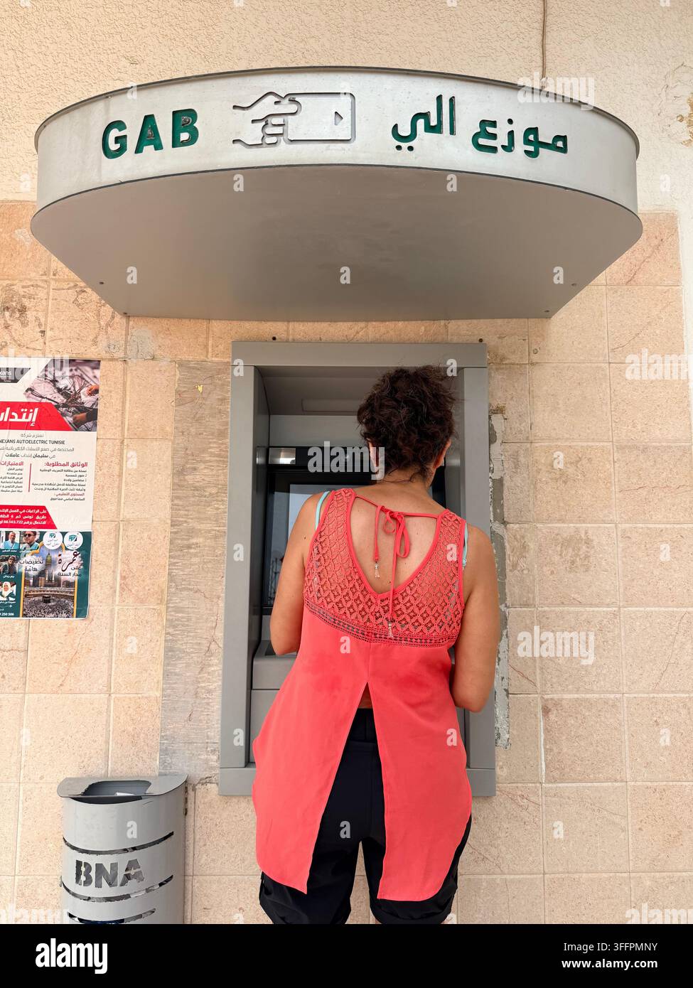 Frau, die Bargeld von einem Geldautomaten in Tunesien abhebt, ein konzeptionelles Bild des alltäglichen Bankwesens, des Finanzzugangs in der Maghreb-Region - Smartphone-aufgenommenes Stockfoto