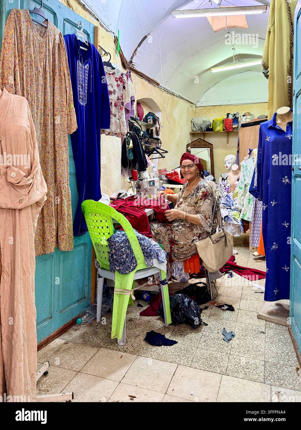 Frauen-Näherin arbeitet in einem kleinen Bekleidungs- und Schneiderei-Shop in der UNESCO-geschützten Medina von Sousse, Tunesien - Smartphone-aufgenommenes Stockfoto