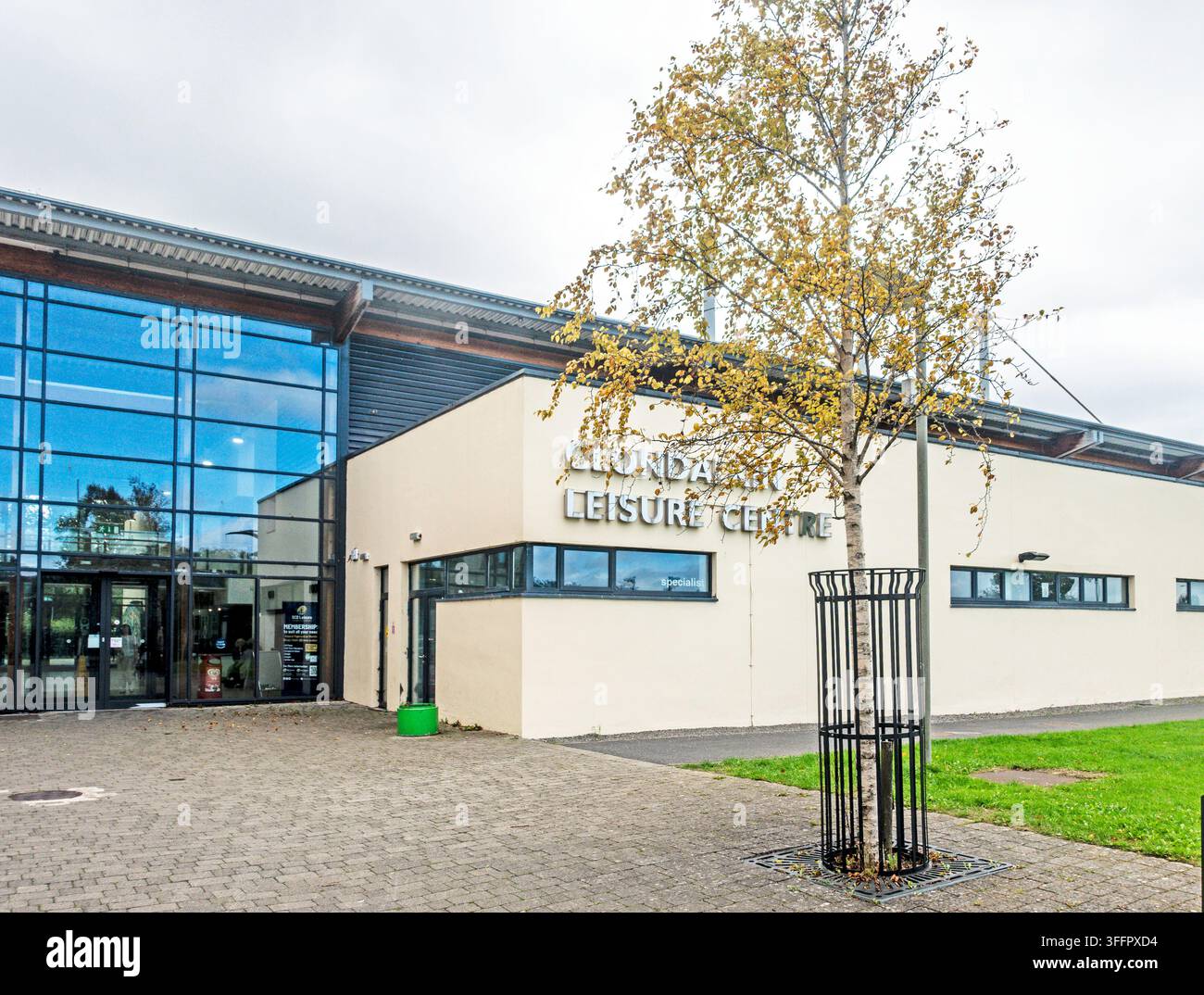 Außenansicht des Clondalkin Leisure Centre mit moderner Glasfassade, gepflastertem Vorplatz und einem jungen Baum in Clondalkin, West-Dublin. Stockfoto