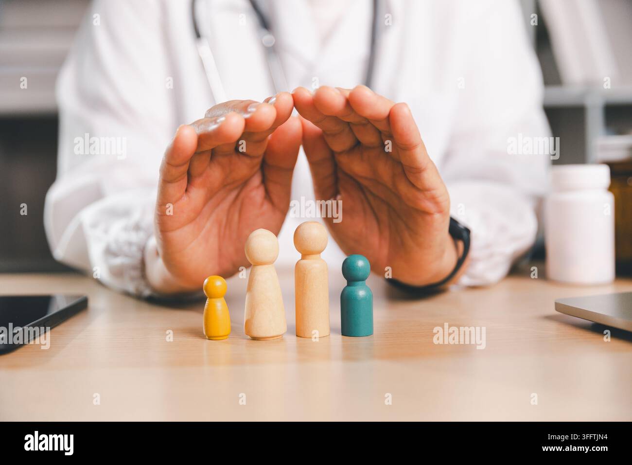 Gesundheitsfachkraft schützt hölzerne Familienfiguren mit beiden Händen, symbolisiert Familienkrankenversicherung, medizinischen Schutz, Pflege, Sicherheit Stockfoto