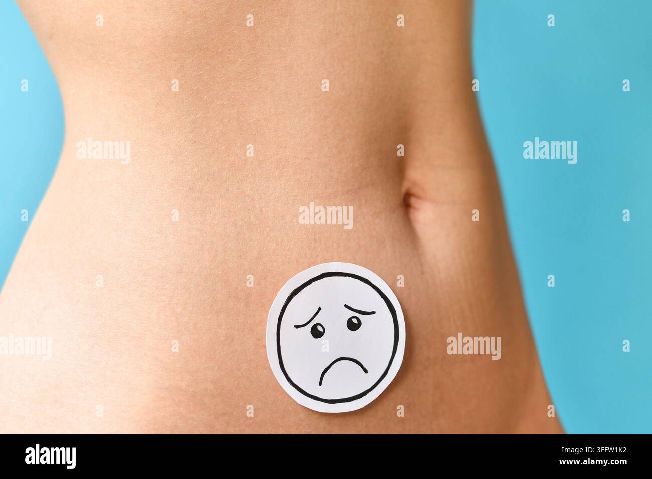 Trauriges Gesicht auf dem Bauch einer Frau, das Menstruationsschmerzen, Endometriose, Fruchtbarkeitsprobleme und reproduktive Gesundheitsprobleme vor blauem Hintergrund symbolisiert Stockfoto