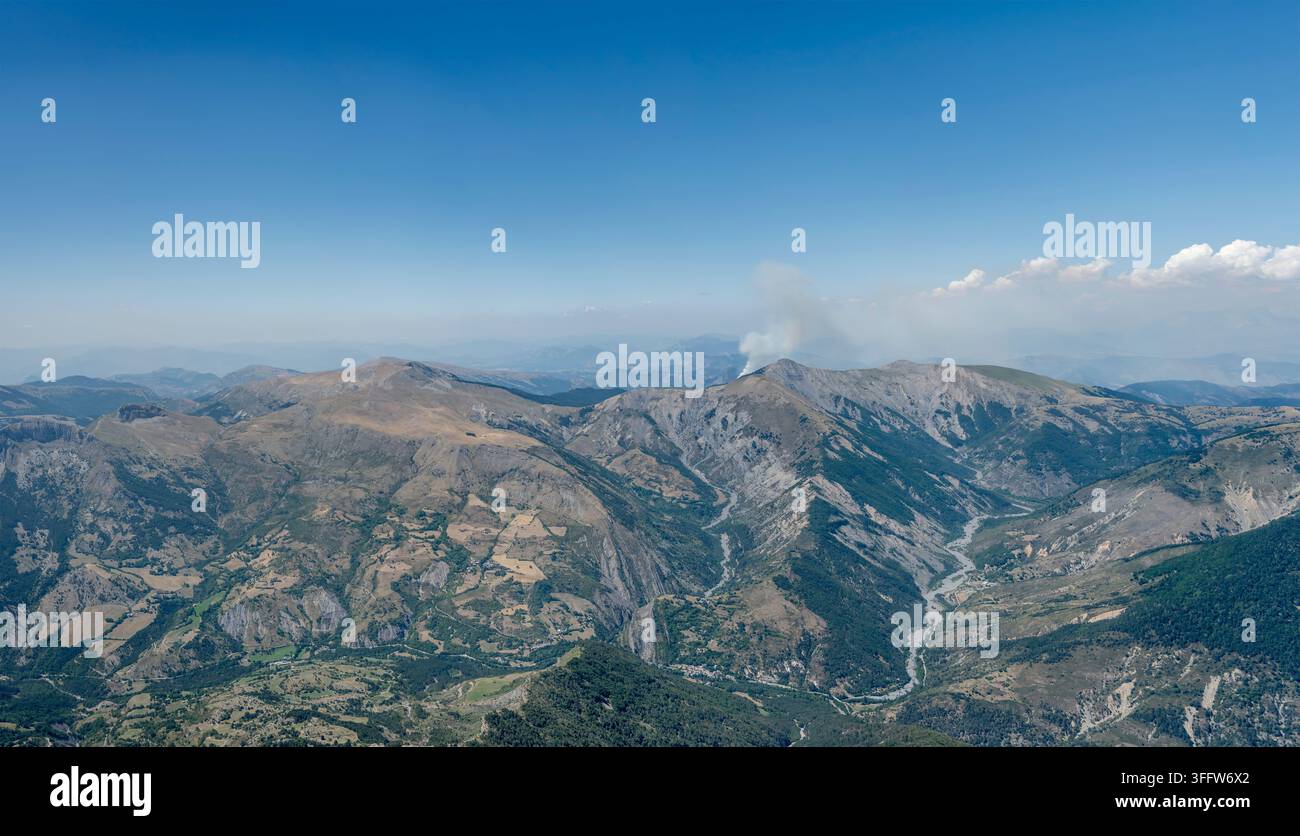 Luftpanoramablick auf eine Landschaft mit Waldbrandrauch und Blick auf die Bergkette des Blayeul-Gipfels von Südwesten, aufgenommen von einem Segelflugzeug im hellen Sommerlicht Stockfoto