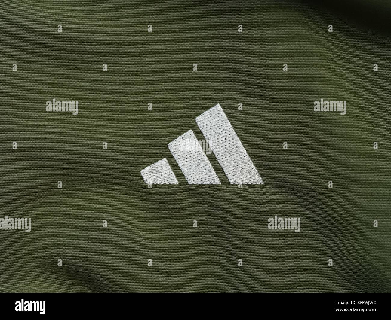 Tambow, Russische Föderation - 03. September 2026 Ein weißes besticktes Adidas-Leistungslogo auf einem dunklen khakifarbenen Sportbekleidungsstoffhintergrund. Stockfoto