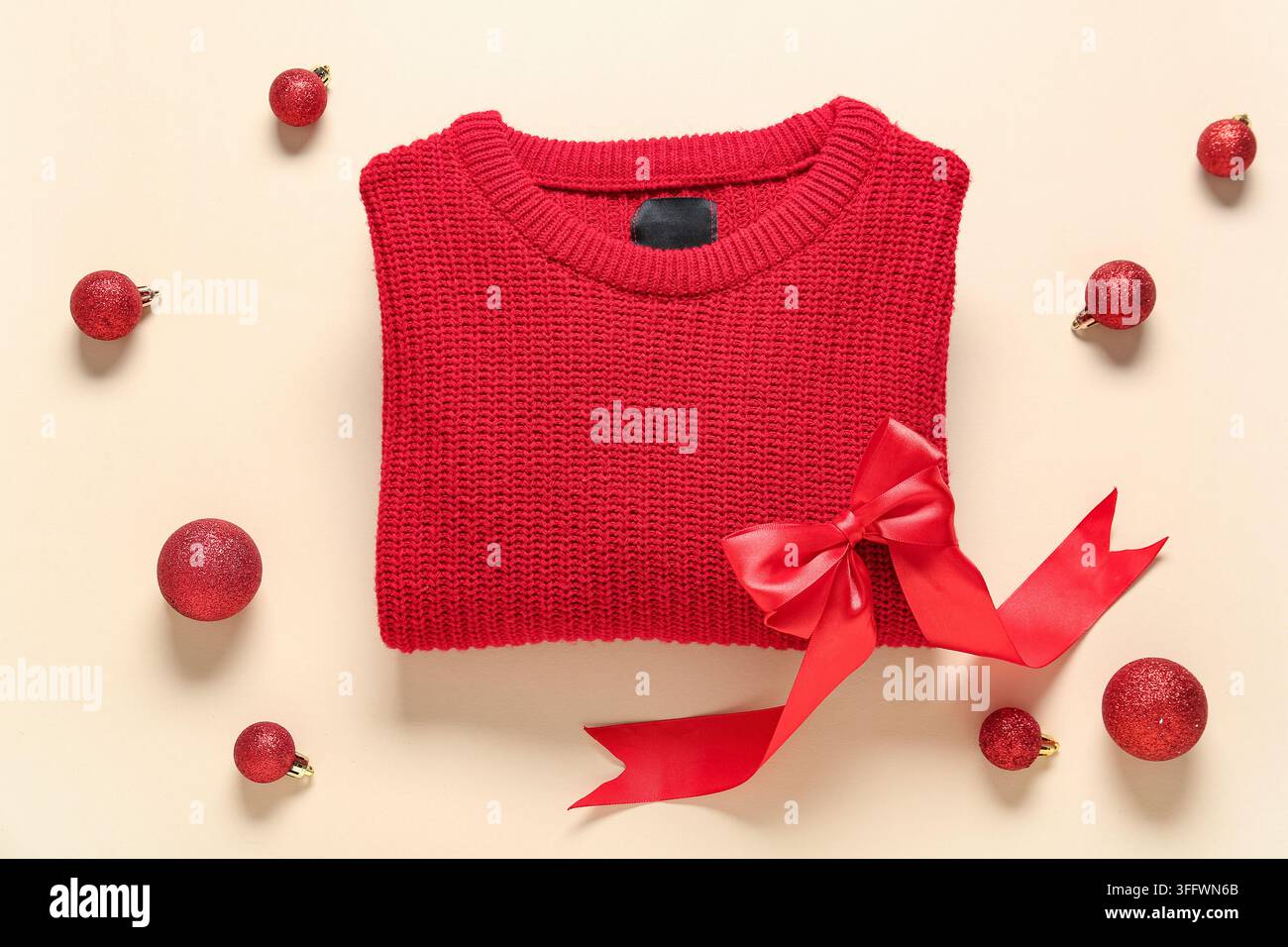 Weihnachtsgeschenk-Einkäufe und Feiertagsmode, roter Strickpullover mit Schleifenband und festlichen Ornamenten auf beigem Hintergrund für saisonale Verkäufe Stockfoto