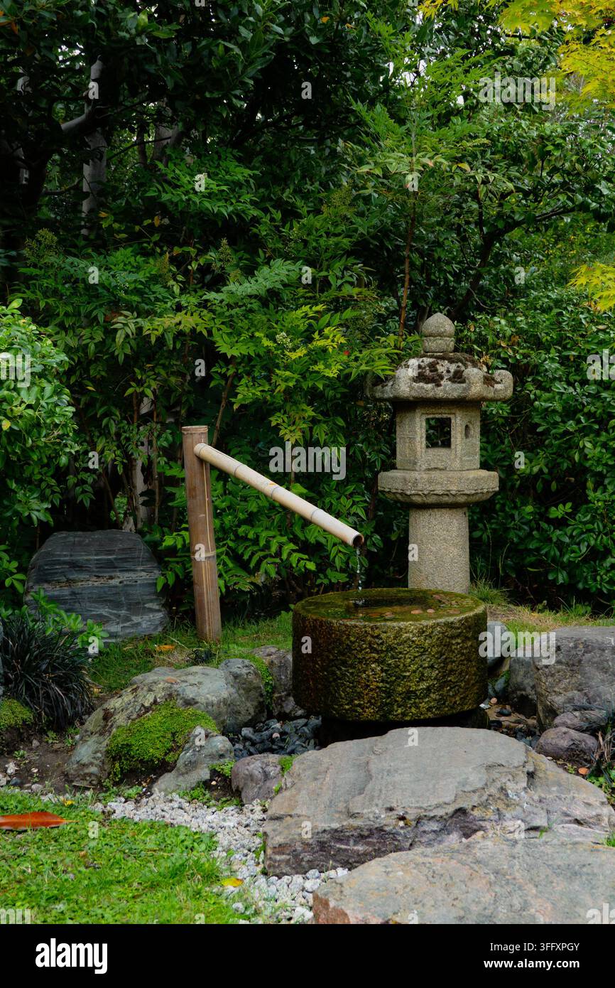 Traditionelles japanisches Steinwasserspülbecken (tsukubai) mit Bambusauslauf im Kyoto-Garten, Holland Park, London, England, UK Stockfoto