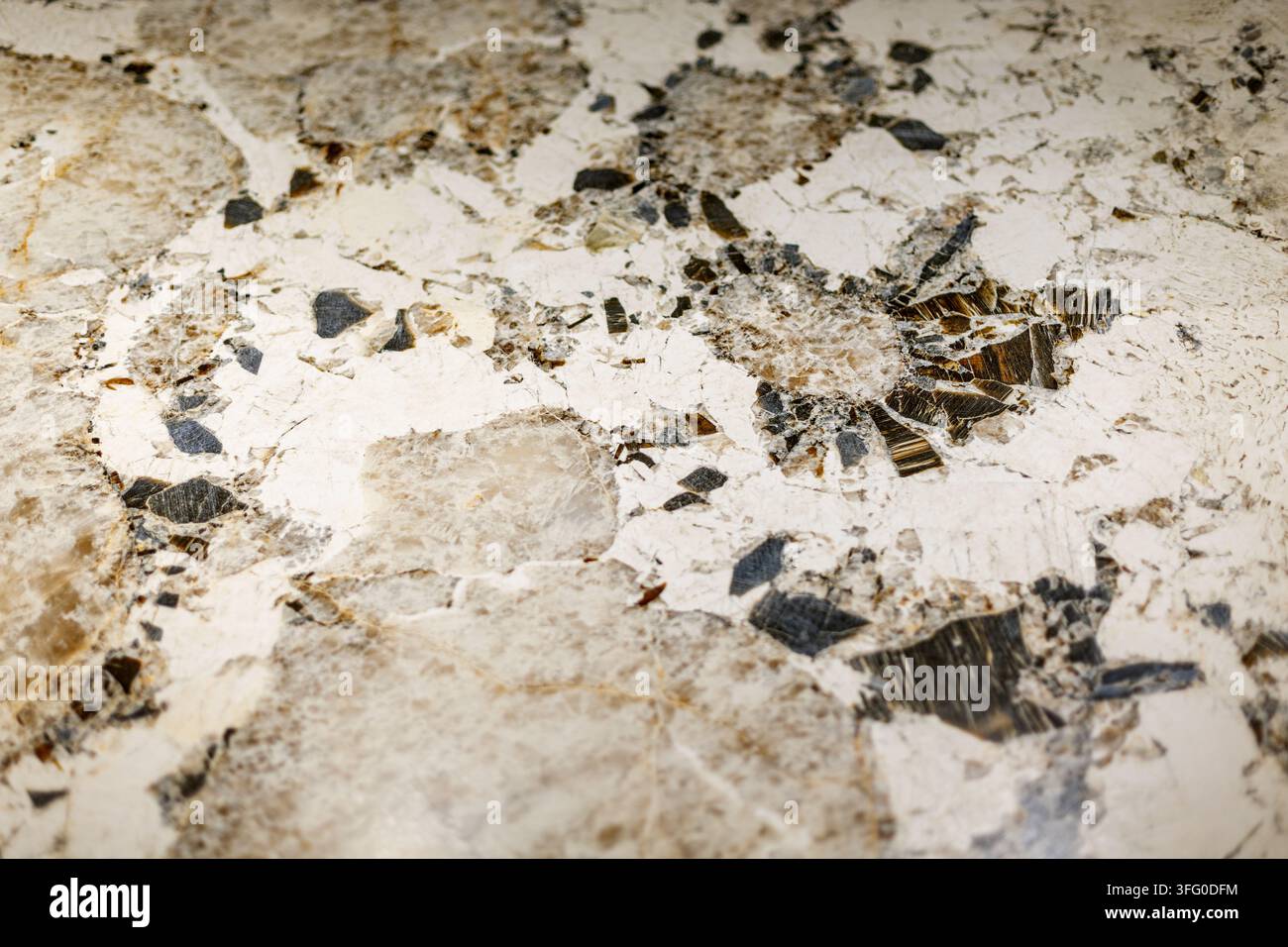 Kristalliner Granitstein mit dunklen Mineralinklusionen. Nahaufnahme von weißem und beigem kristallinem Stein mit dunklen Mineralfragmenten und natürlichem Stockfoto