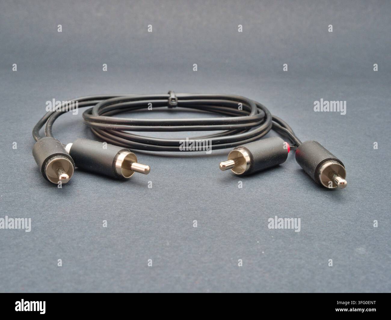 RCA-Audiokabel auf dunklem Hintergrund – Ein schwarzes Stereo-RCA-Audiokabel mit roten und weißen Steckern ist ordentlich aufgerollt und auf einer dunkelgrauen Oberfläche befestigt. Stockfoto